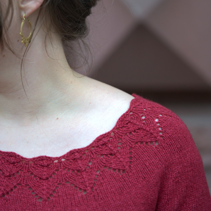 A red sweater with a wide neckline that has a beautiful lace edge.